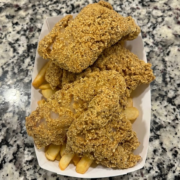 Crispy fried fish fillets and golden french fries served in a white paper tray on a speckled countertop.