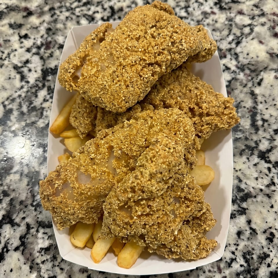 Crispy fried fish fillets and golden french fries served in a white paper tray on a speckled countertop.