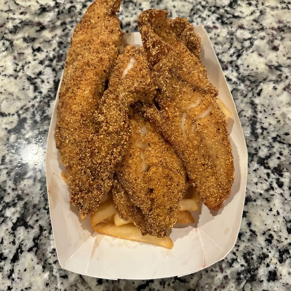 Crispy fried fish fillets and golden french fries served in a white paper tray on a granite counter.