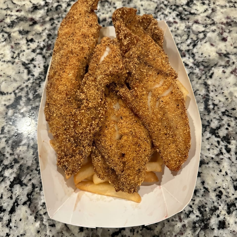 Crispy fried fish fillets and golden french fries served in a white paper tray on a granite counter.