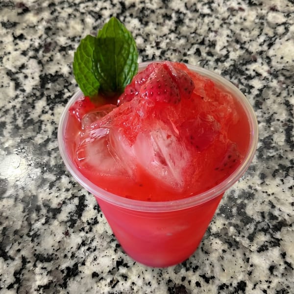 Bright red drink with ice, topped with fruit pulp and a mint sprig on a speckled countertop.