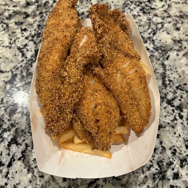 Crispy fried fish fillets with french fries in a white paper tray on a speckled countertop.